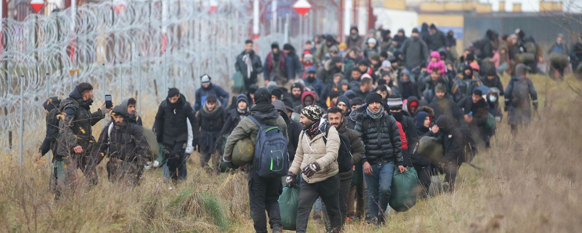 A group of migrants walk near a barbed wire fence while moving toward a makeshift camp on the Belarusian-Polish border in the Grodno region, Belarus November 12, 2021. Leonid Scheglov/BelTA/Handout via REUTERS ATTENTION EDITORS - THIS IMAGE HAS BEEN SUPPLIED BY A THIRD PARTY. NO RESALES. NO ARCHIVE. MANDATORY CREDIT. A group of migrants walk near a barbed wire fence while moving toward a makeshift camp on the Belarusian-Polish border in the Grodno region, Belarus November 12, 2021. Leonid Scheglov/BelTA/Handout via REUTERS ATTENTION EDITORS - THIS IMAGE HAS BEEN SUPPLIED BY A THIRD PARTY. NO RESALES. NO ARCHIVE. MANDATORY CREDIT. - Sputnik International, 1920, 21.11.2021