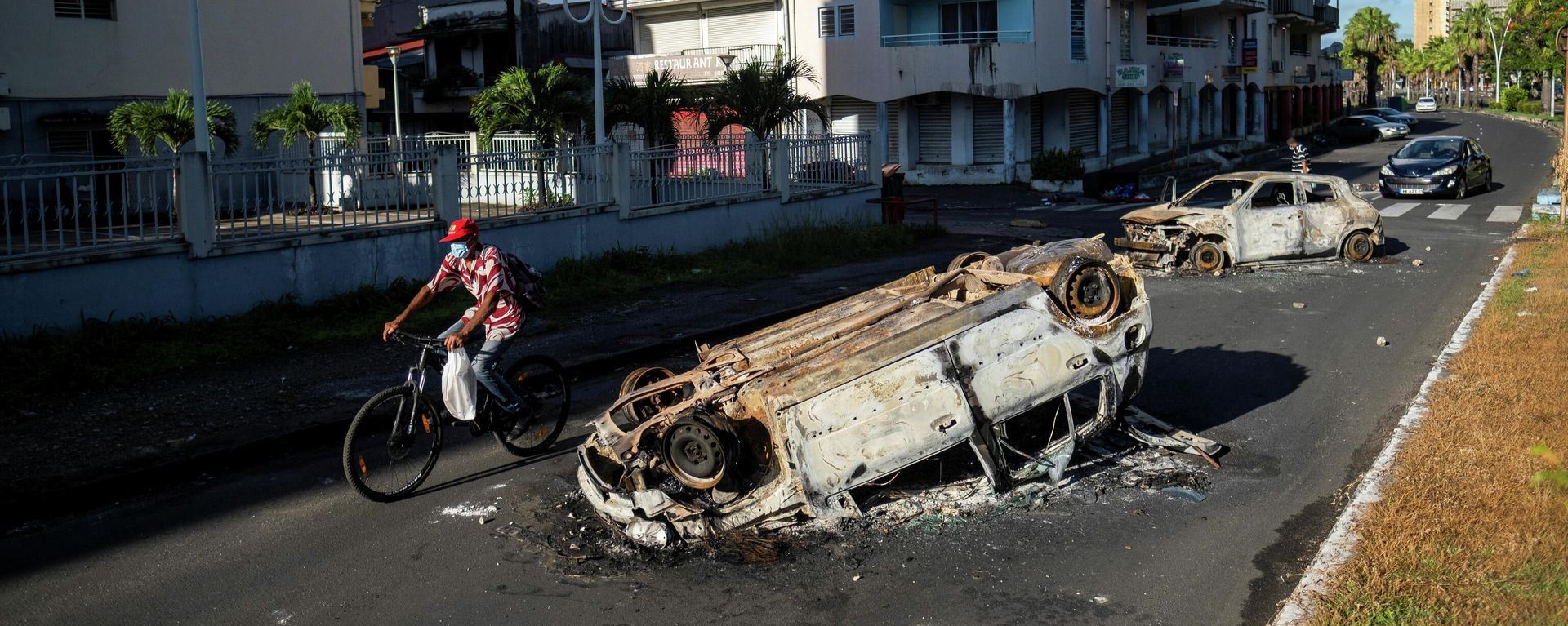 A man rides his bicycle past burned cars after violent demonstrations which broke out over coronavirus disease (COVID-19) protocols, in Pointe-a-Pitre, Guadeloupe November 21, 2021 A man rides his bicycle past burned cars after violent demonstrations which broke out over coronavirus disease (COVID-19) protocols, in Pointe-a-Pitre, Guadeloupe November 21, 2021 - Sputnik International, 1920, 23.11.2021