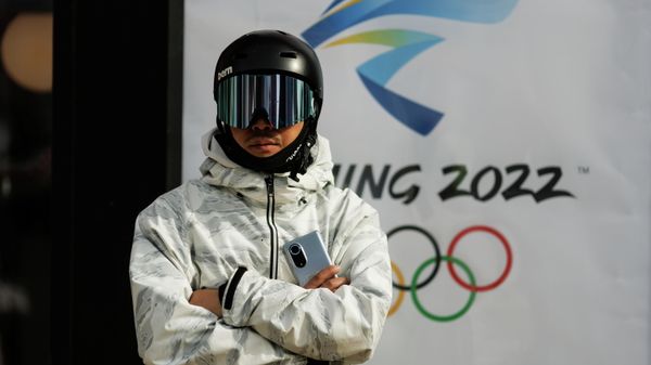 A snowboarder stands in front of the logo of the Beijing 2022 Winter Olympics in Zhangjiakou, Hebei province, China, November 20, 2021 - Sputnik International