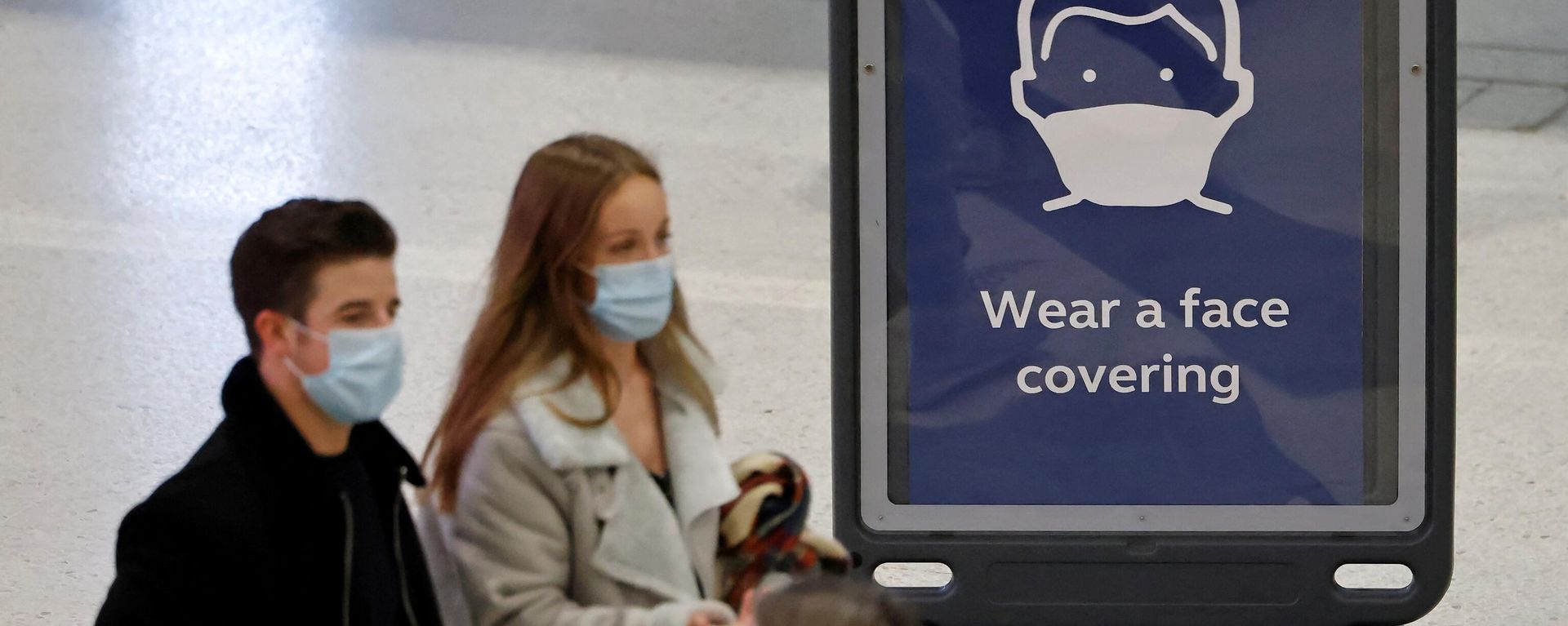 Pedestrians, some wearing face coverings to combat the spread of Covid-19, walk past a sign asking commuters to Wear a face covering, at Liverpool Street train station in central London on December 18, 2021. - Sputnik International, 1920, 19.08.2023