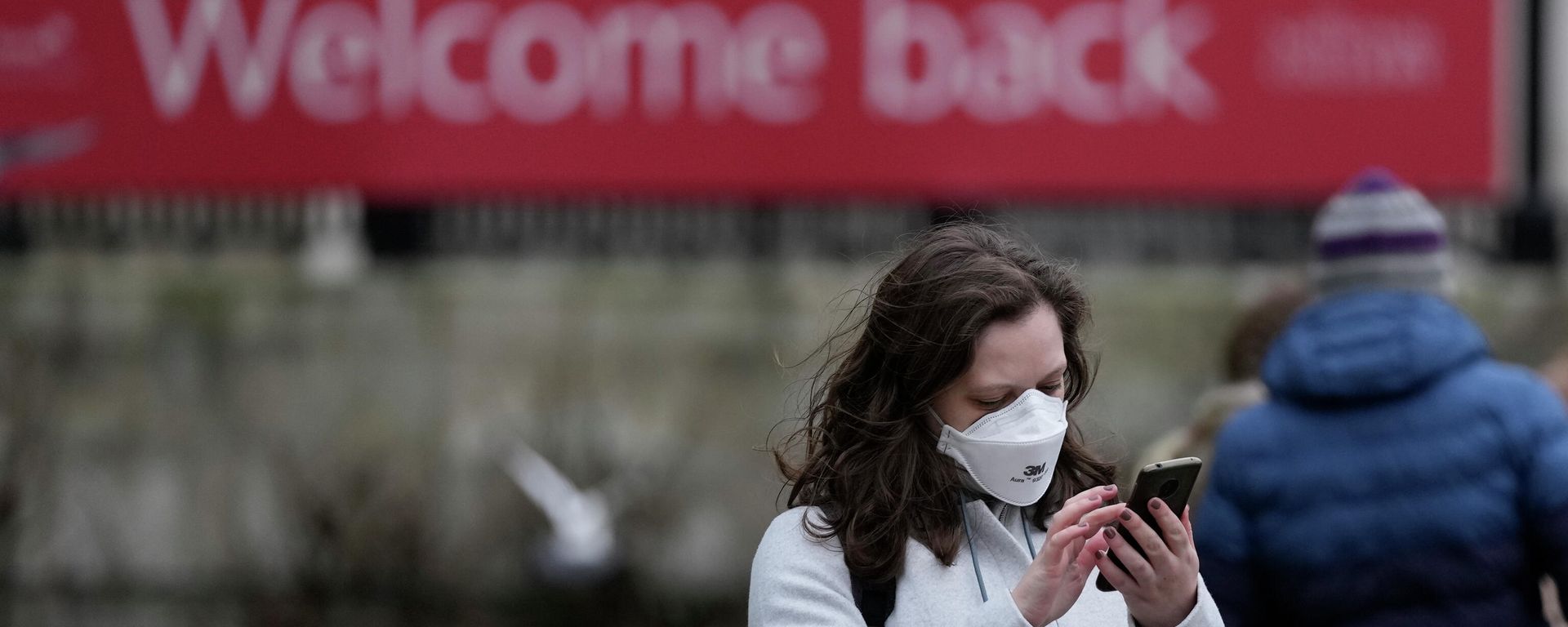 A woman wearing a mask to protect against the coronavirus looks at her phone in Trafalgar Square, in London - Sputnik International, 1920, 12.01.2022