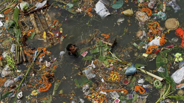 A man searches for reusable material in the waters of the River Kuakhai polluted with offerings thrown by devotees after the immersion of idols of Hindu deities in Bhubaneswar, India, Friday, Sept. 18, 2015 - Sputnik International