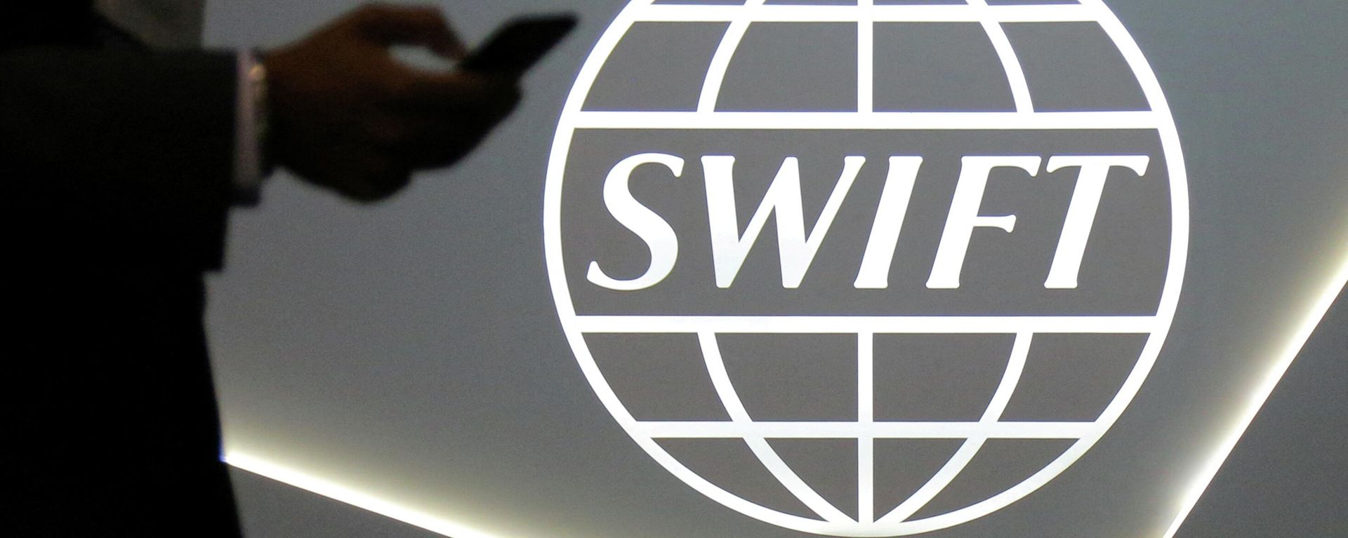 : A man using a mobile phone passes the logo of global secure financial messaging services cooperative SWIFT at the SIBOS banking and financial conference in Toronto, Ontario, Canada October 19, 2017 : A man using a mobile phone passes the logo of global secure financial messaging services cooperative SWIFT at the SIBOS banking and financial conference in Toronto, Ontario, Canada October 19, 2017 - Sputnik International, 1920, 27.02.2022