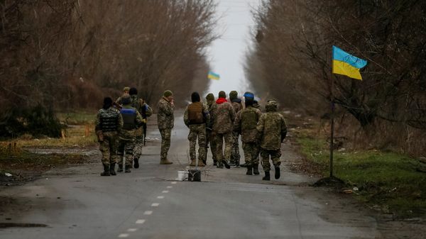 Ukrainian service members walk near a Ukrainian flag in the village of Kozarovychi, in Kyiv region, Ukraine April 2, 2022 - Sputnik International