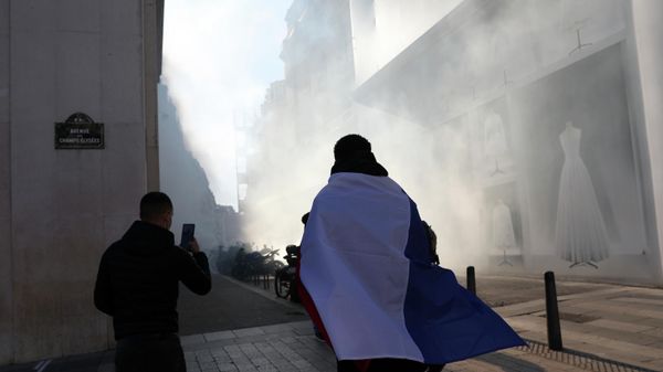 A protester leaves the Champs-Elysees avenue though tear gas during a protest, Saturday, Feb.12, 2022 in Paris. - Sputnik International