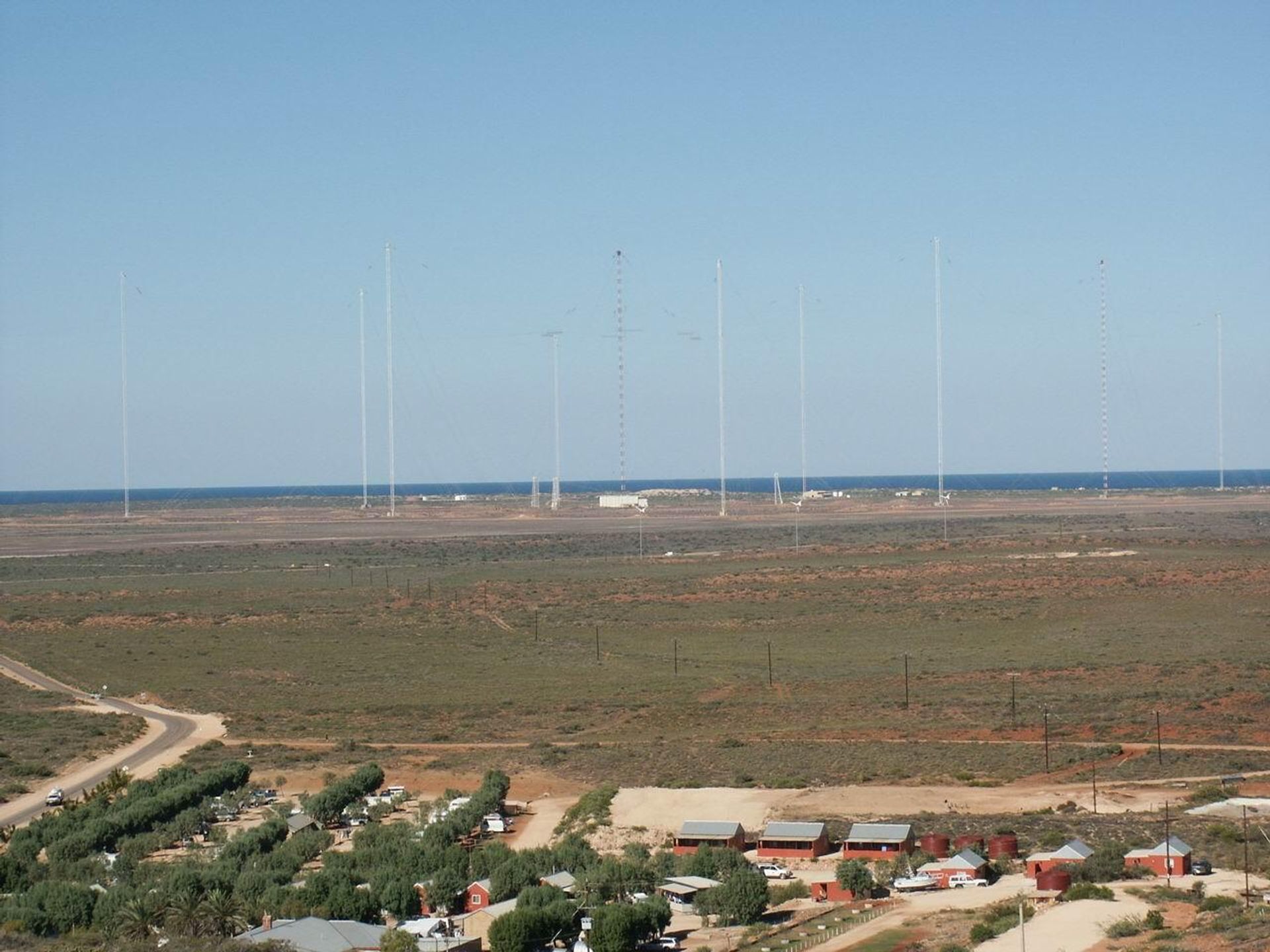 Naval Communication Station Harold E. Holt near Exmouth, Western Australia. The radio masts are part of a large wire antenna which is used to transmit very low frequency (VLF) radio waves to communicate with submerged submarines. This type of antenna is known as a Goliath, a type of umbrella antenna, but has been heavily modified. It consists of a ring of steel masts which support a network of horizontal cables radiating from the central mast. The central mast acts as the radiating element, while the horizontal cables serve as a capacitive top-load, creating a large capacitor with the ground. This serves to increase the current in the central radiator, increasing the radiated power. Naval Communication Station Harold E. Holt near Exmouth, Western Australia. The radio masts are part of a large wire antenna which is used to transmit very low frequency (VLF) radio waves to communicate with submerged submarines. This type of antenna is known as a Goliath, a type of umbrella antenna, but has been heavily modified. It consists of a ring of steel masts which support a network of horizontal cables radiating from the central mast. The central mast acts as the radiating element, while the horizontal cables serve as a capacitive top-load, creating a large capacitor with the ground. This serves to increase the current in the central radiator, increasing the radiated power. - Sputnik International, 1920, 16.05.2022