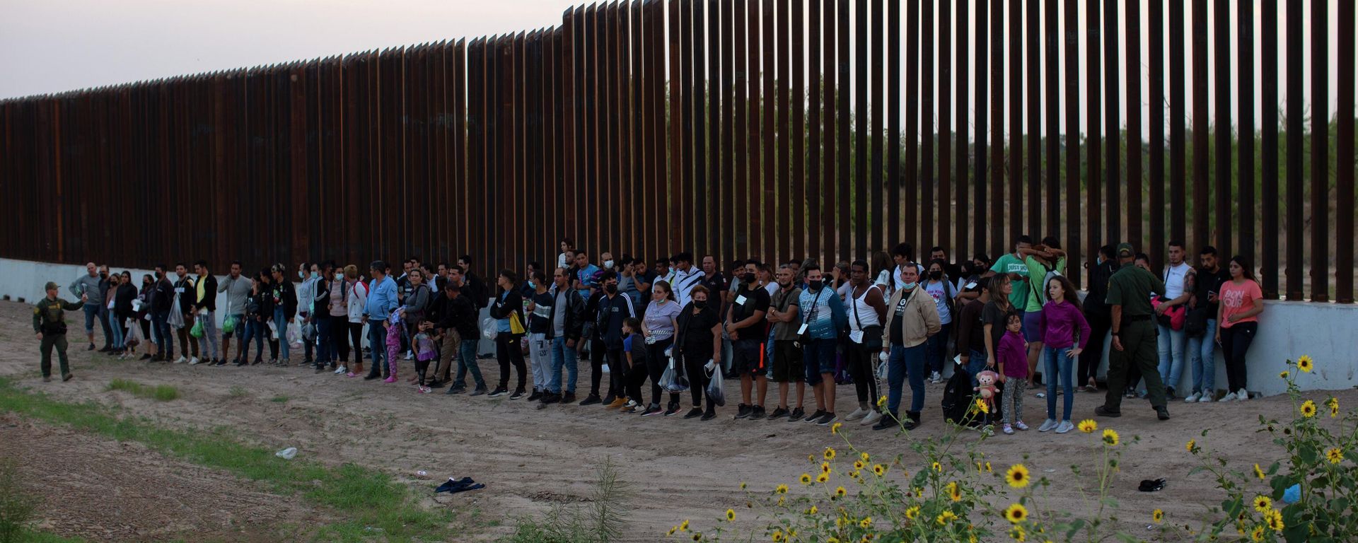 A group of migrants stand next to the border wall as they wait to get taken away by the Border Patrol in Eagle Pass, Texas, Saturday, May 21, 2022 A group of migrants stand next to the border wall as they wait to get taken away by the Border Patrol in Eagle Pass, Texas, Saturday, May 21, 2022 - Sputnik International, 1920, 15.11.2022