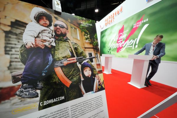 A man sets a tribune at a stand of the Russian People's Front movement with a poster showing a Donbass serviceman with two children, at the St. Petersburg International Economic Forum in St. Petersburg. - Sputnik International