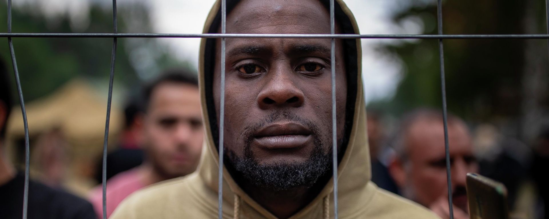 A migrant stands by the fence at the newly built refugee camp in the Rudninkai military training ground, some 38km (23,6 miles) south from Vilnius, Lithuania, Wednesday, Aug. 4, 2021 - Sputnik International, 1920, 23.11.2023