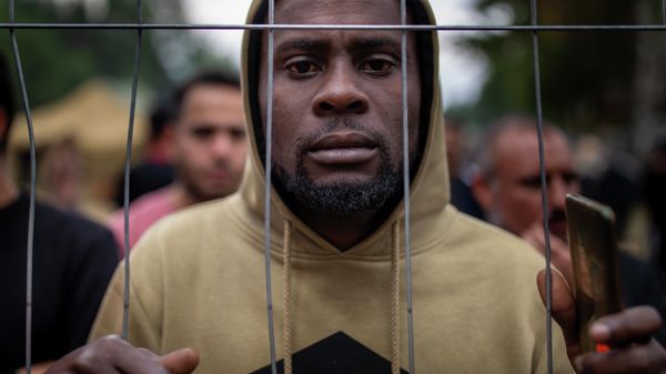 A migrant stands by the fence at the newly built refugee camp in the Rudninkai military training ground, some 38km (23,6 miles) south from Vilnius, Lithuania, Wednesday, Aug. 4, 2021 - Sputnik International