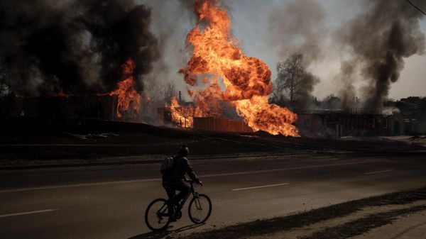 A man rides his bike past flames and smoke rising from a fire following an attack in Kharkiv, Ukraine, Friday, March 25, 2022. - Sputnik International