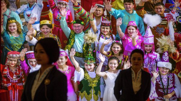 Tour guides stand in front of a large photo depicting different ethnic groups in Xinjiang at the Exhibition of the Fight Against Terrorism and Extremism in Urumqi in northwestern China's Xinjiang Uyghur Autonomous Region, as seen during a government organized visit, on April 21, 2021 - Sputnik International