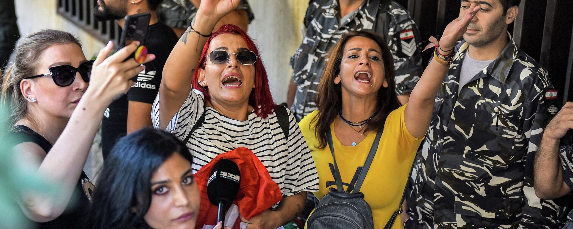 A television reporter looks on as people chant slogans next to security forces standing guard outside a branch of LGB Bank, reportedly held up by a depositor seeking access to his own savings according to a bank employee, in Ramlet al-Bayda area in the capital Beirut on September 16, 2022.  - Sputnik International, 1920, 16.09.2022