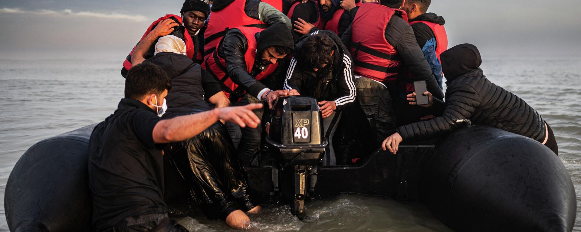 Migrants try to start an outboard engine after boarding a smuggler's boat on the beach of Gravelines, near Dunkirk, northern France on October 12, 2022, in a attempt to cross the English Channel Migrants try to start an outboard engine after boarding a smuggler's boat on the beach of Gravelines, near Dunkirk, northern France on October 12, 2022, in a attempt to cross the English Channel - Sputnik International, 1920, 14.11.2022