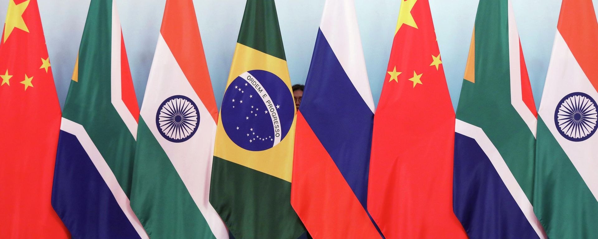 Staff worker stands behind national flags of Brazil, Russia, China, South Africa and India to tidy the flags ahead of a group photo during the BRICS Summit at the Xiamen International Conference and Exhibition Center in Xiamen, southeastern China's Fujian Province, Monday, Sept. 4, 2017. - Sputnik International, 1920, 24.10.2025