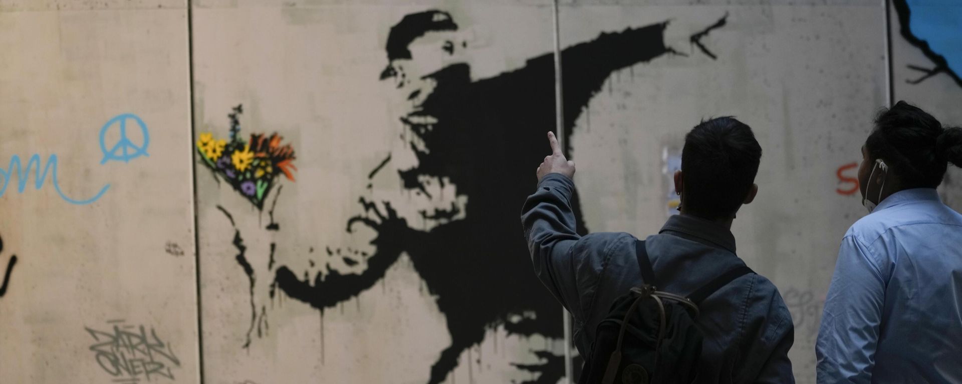 Visitors walk past Flower Thrower, a reproduction of a mural by British artist Banksy, during the unveiling of the The World of Banksy, The Immersive Experience exhibition, in Milan, Italy, Thursday, Dec. 2, 2021. Visitors walk past Flower Thrower, a reproduction of a mural by British artist Banksy, during the unveiling of the The World of Banksy, The Immersive Experience exhibition, in Milan, Italy, Thursday, Dec. 2, 2021. - Sputnik International, 1920, 19.11.2022