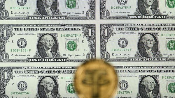 An illustration picture taken in London on May 8, 2022, shows a gold plated souvenir cryptocurrency Tether (USDT) coin arranged beside a screen displaying US dollar notes. - Tether (USDT) is an Ethereum token known as a stablecoin that is pegged to the value of the US dollar, and is currently the largest stablecoin with a market value of USD 83 billion dollars.  - Sputnik International