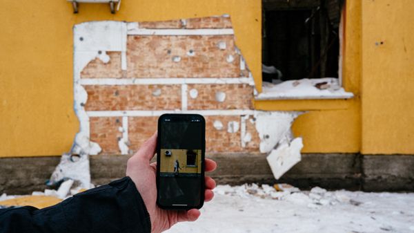This photograph taken on December 3, 2022 shows a mobile phone with Banksy's work on the screen in front of a cut off of the wall of a damaged building from where a group of people tried to steal this work of the famous British artist in the town of Gostomel, near Kiev. - Sputnik International