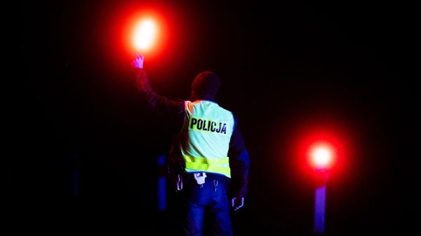 A police officer holds up lights to check vehicles entering the state of emergency area at a checkpoint near the village of Bialowieza, eastern Poland, close to the Polish-Belarusian border, on November 21, 2021 - Sputnik International