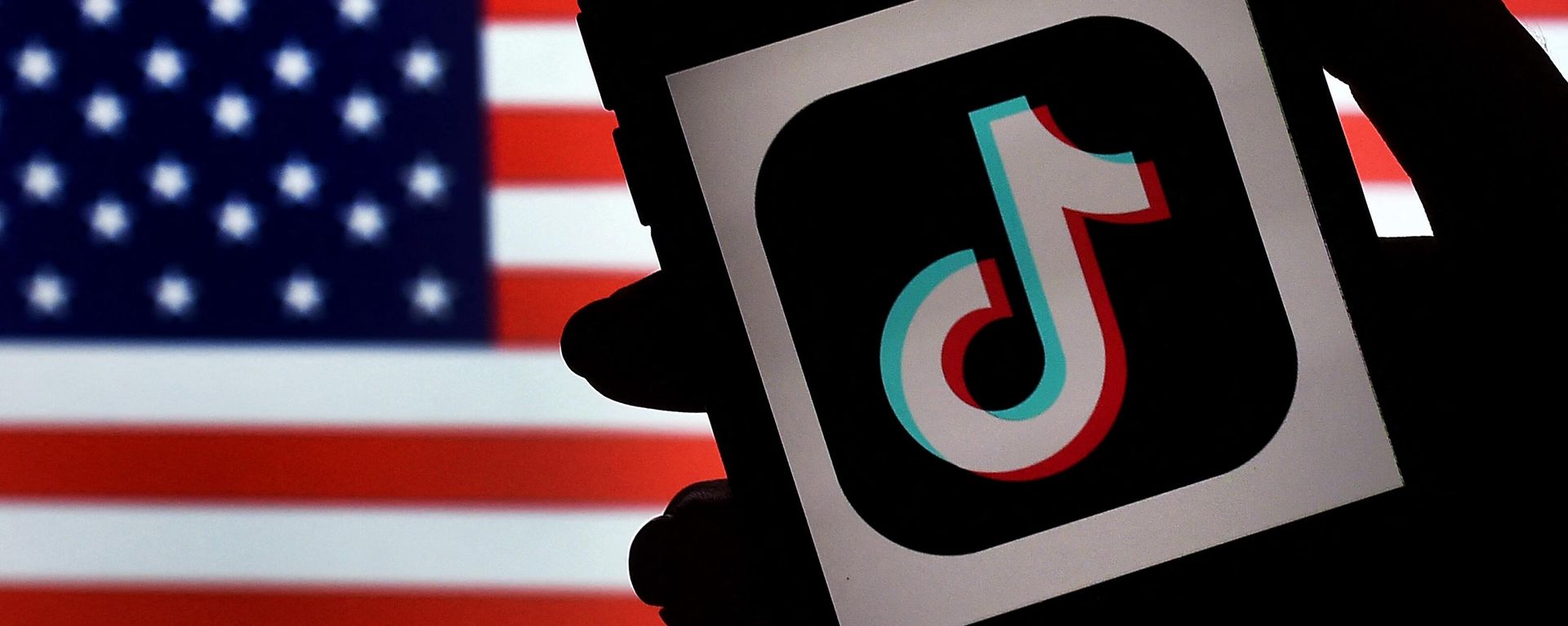 The social media application logo, TikTok is displayed on the screen of an iPhone on an American flag background.  - Sputnik International, 1920, 03.01.2023
