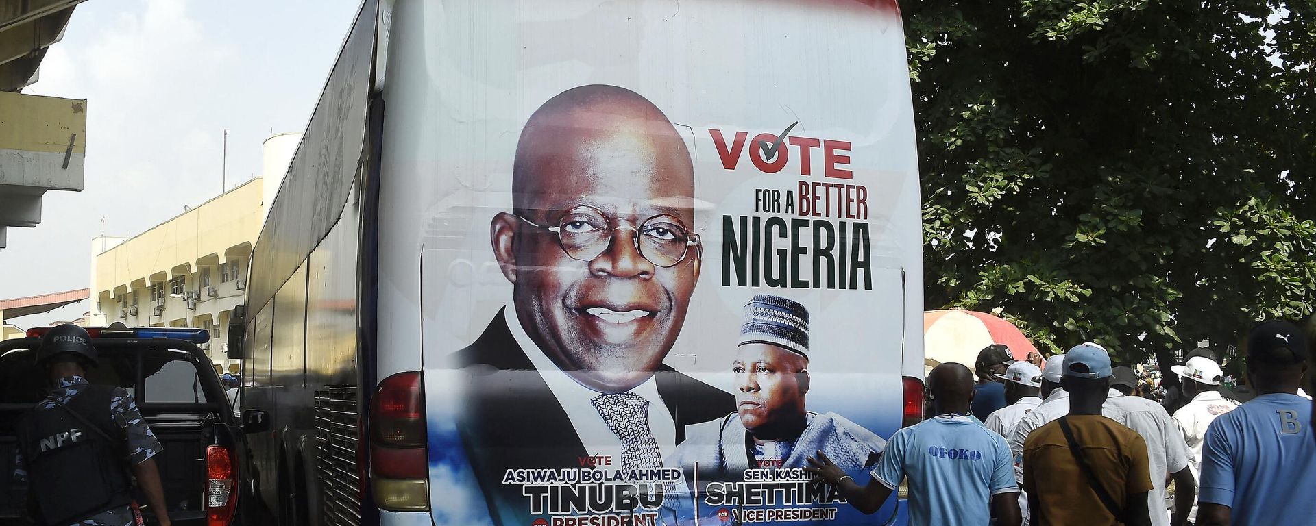 Members of the public stand behind a campaign poster of presidential candidate of All Progressives Congress (APC) Bola Tinubu and runningmate Abdullahi Shettima, displayed on a bus, during a party campaign rally at Teslim Balogun Stadium in Lagos, on November 26, 2022 Members of the public stand behind a campaign poster of presidential candidate of All Progressives Congress (APC) Bola Tinubu and runningmate Abdullahi Shettima, displayed on a bus, during a party campaign rally at Teslim Balogun Stadium in Lagos, on November 26, 2022 - Sputnik International, 1920, 29.12.2022
