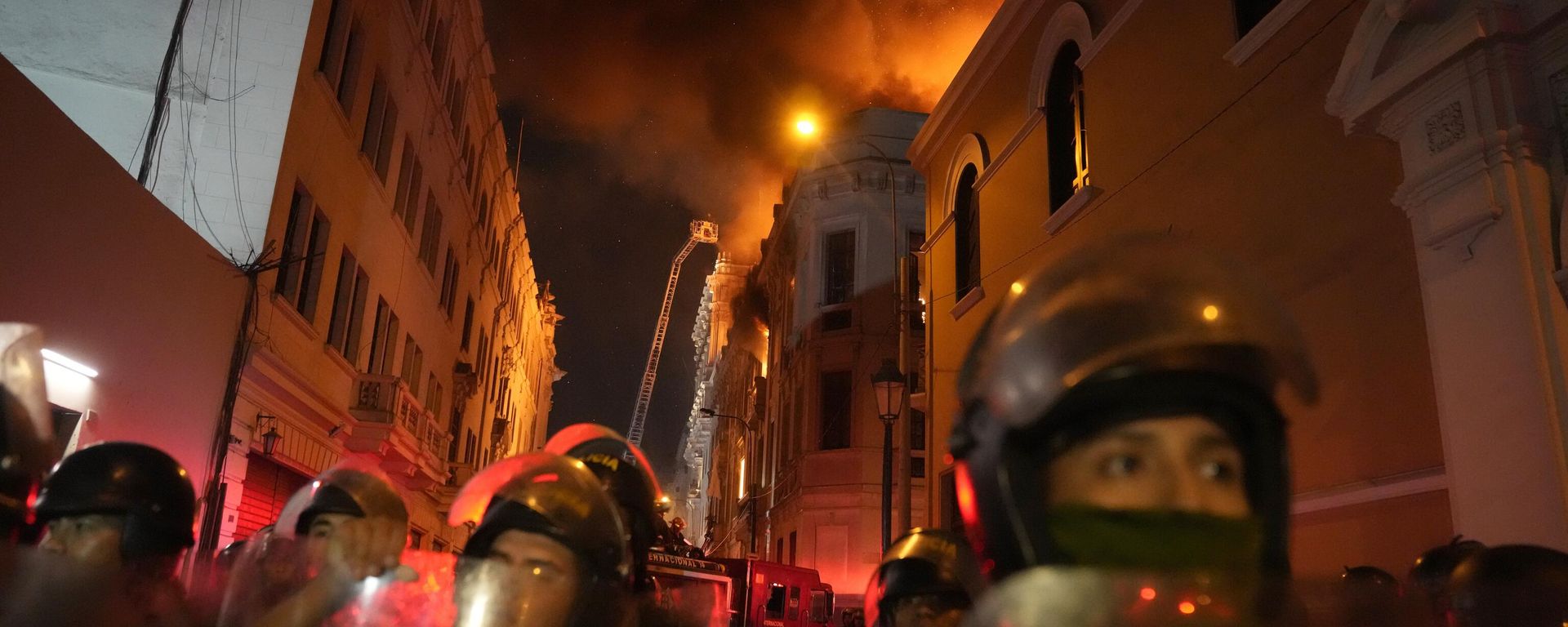 Police in riot gear block a street as a building burns behind them after a day a day of clashes with anti-government protesters in Lima, Peru, Thursday, Jan. 19, 2023. Protesters are seeking immediate elections, Boluarte's resignation, the release of ousted President Pedro Castillo and justice for protesters killed in clashes with police. - Sputnik International, 1920, 20.01.2023