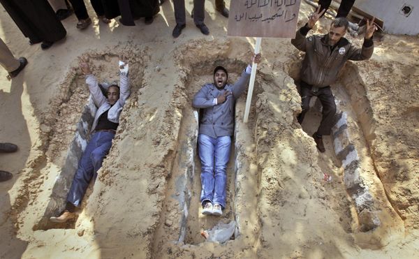 Residents lie in open graves and make the victory sign, to show their willingness to sacrifice themselves to the cause at a park in the main square in Zawiya, 30 miles (50 kilometers) west of Tripoli, in Libya on Sunday 27 February 2011. The placard bears the message: "There is no God but Allah. Martyrs are God's beloved." - Sputnik International