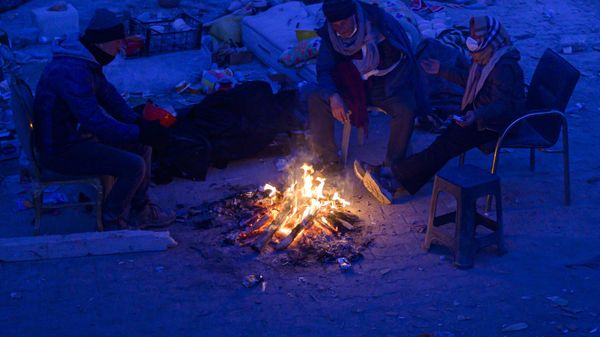 Local residents waiting for news of their relatives, sit by a bonfire near the rubble of collapsed buildings in Turkish Hatay, on February 14, 2023, after a 7.8-magnitude earthquake struck the country's south-east.  - Sputnik International