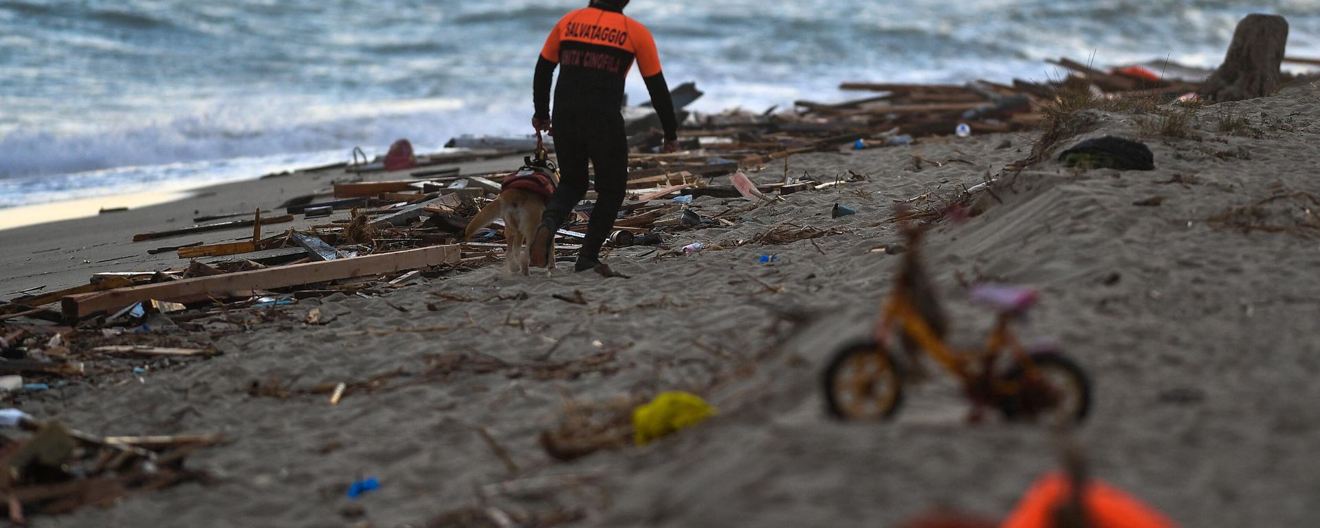 A member of the cynophile police and his dog patrol the beach on February 26, 2023 in Steccato di Cutro, south of Crotone, where debris of a shipwreck were washed ashore after a migrants' boat sank off Italy's southern Calabria region - Sputnik International, 1920, 27.02.2023