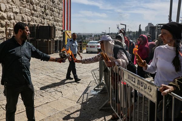 A man who obtained the Holy Fire from the Church of the Holy Sepulcher in Jerusalem lights the candles of Christian worshippers waiting behind a barrier set up by Israeli security forces, during Orthodox Christian Easter Saturday celebrations. - Sputnik International