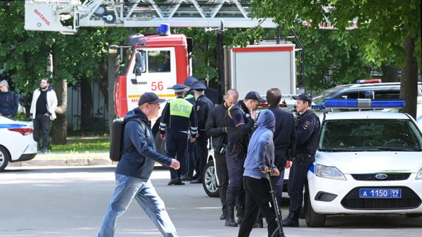People walk past emergency personnel outside a residential building damaged in a drone attack in Moscow - Sputnik International