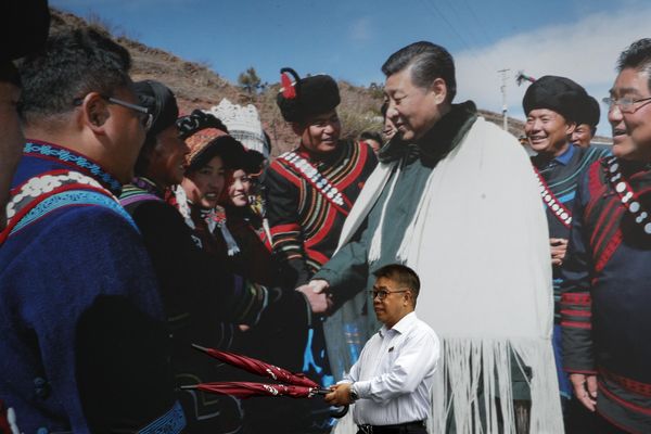 A man carrying umbrellas walks by a photo showing Chinese President Xi Jinping meeting with ethnic minorities on display at a hotel in Chengdu in southwest China's Sichuan province. - Sputnik International