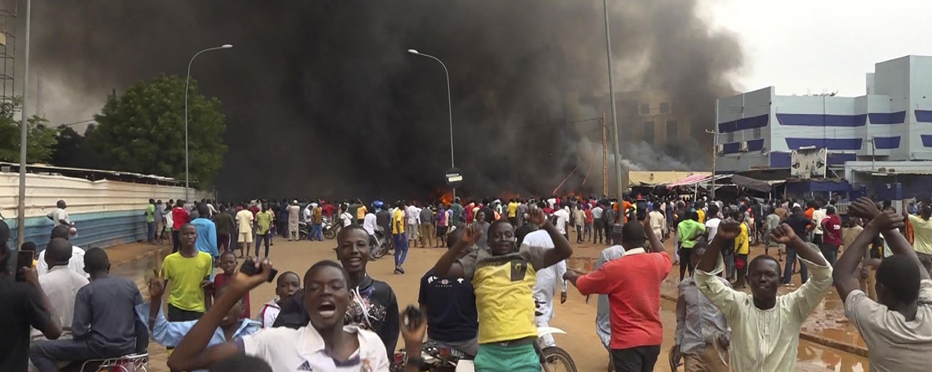 With the headquarters of the ruling party burning in the back, supporters of mutinous soldiers demonstrate in Niamey, Niger - Sputnik International, 1920, 02.08.2023