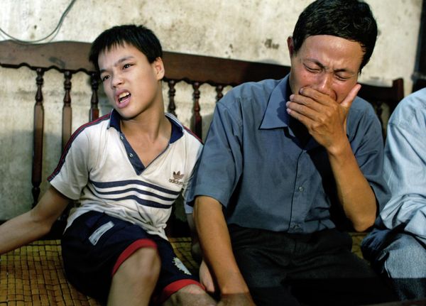 Nguyen Van Quy, 49, weeps while sitting with his son Nguyen Quang Trung, 17, at his house in Hai Phong, Vietnam on July 2004. Quy believes his children's birth defects were caused by Agent Orange that he was exposed to during the Vietnam War.  - Sputnik International