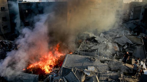 Palestinians stand on the rubble of a levelled building as smoke and fire rise from the destruction following an Israeli strike in Gaza City on October 26, 2023. - Sputnik International