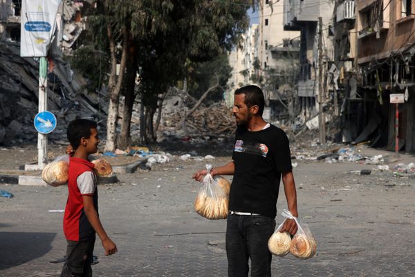 People carry bags of bread as they stand in front of a building destroyed by Israeli strikes in Gaza City. - Sputnik International