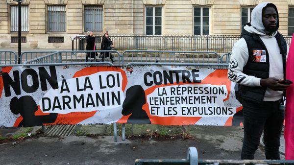 A protestor stand next to a banner reading No to the Darmanin law (L) and Against repression, confinement and expulsions (R) during a demonstration called by associations and NGOs for the defence of immigrants and by the French union General Confederation of Labour (CGT), in front of the National Assembly in Paris on December 11, 2023, against a draft law to control immigration. A controversial draft law to control immigration arrives at the French National Assembly for debate but is immediately threatened by a motion of preliminary rejection that could stop the examining of the law on December 11, 2023. - Sputnik International