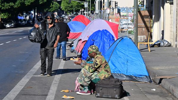 A homeless man sits on a suitcase on the side of a street lined with tents housing the homeless in Downtown Los Angeles on November 22, 2023. - Sputnik International