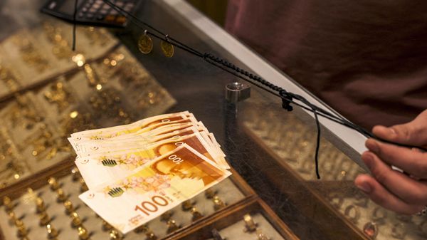 A man holds a string necklace carrying gold ornaments over a counter showing a stack of one-hundred Israeli shekel banknotes at a jeweller's shop in Hebron in the occupied West Bank on October 5, 2023. - Sputnik International