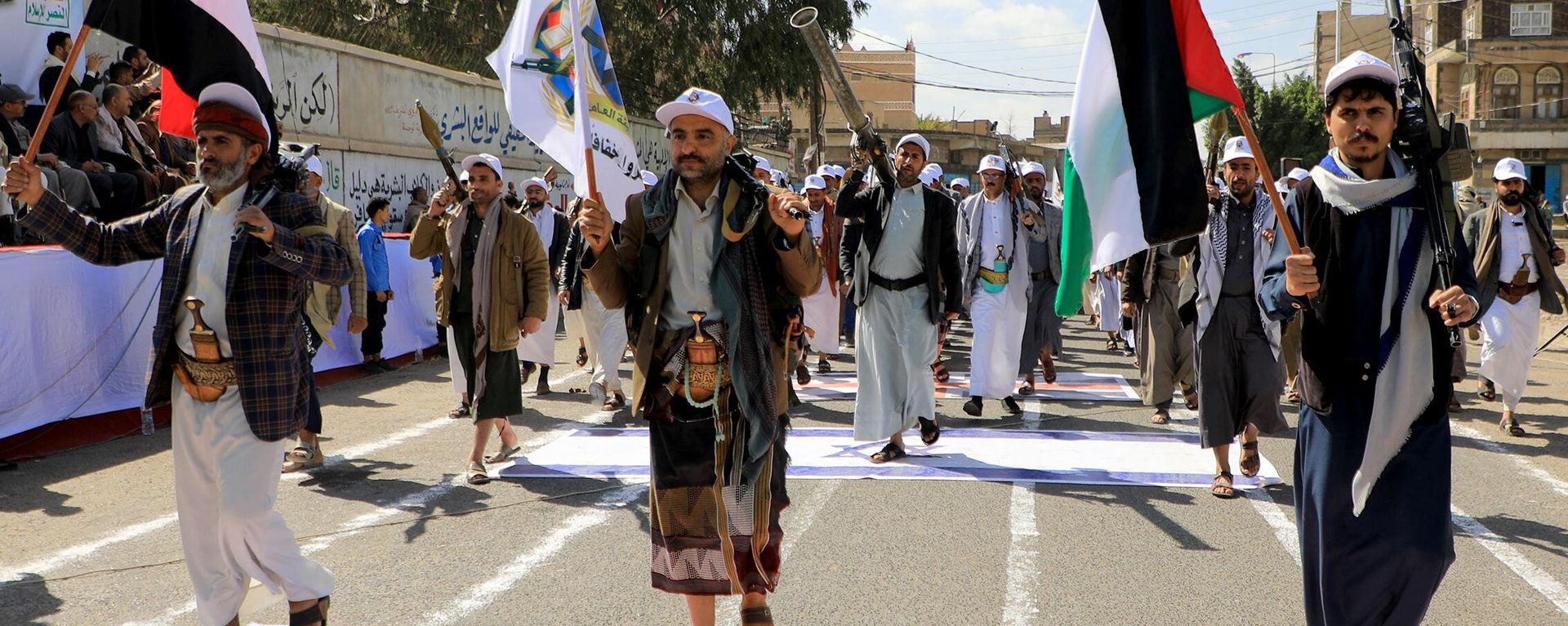 Armed Yemeni men step over a US and an Israeli flag painted on the asphalt in the Houthi-run capital Sanaa, during a march in support of the Palestinians amid ongoing battles between Israel and Hamas militants in the Gaza Strip, on February 29, 2024.  - Sputnik International, 1920, 19.03.2024
