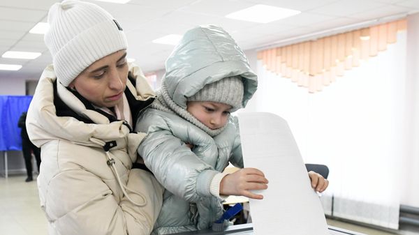 A woman with a child casts her ballot at a polling station during the presidential election in Kirovskoye A woman with a child casts her ballot at a polling station during the presidential election in Kirovskoye - Sputnik International