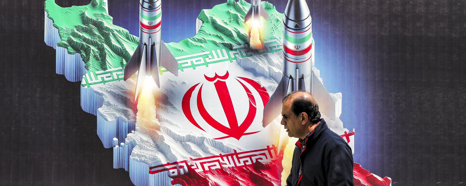 A man walks past a banner depicting missiles launching from a representation of the map of Iran coloured with the Iranian flag in central Tehran on April 15, 2024 - Sputnik International, 1920, 16.05.2024