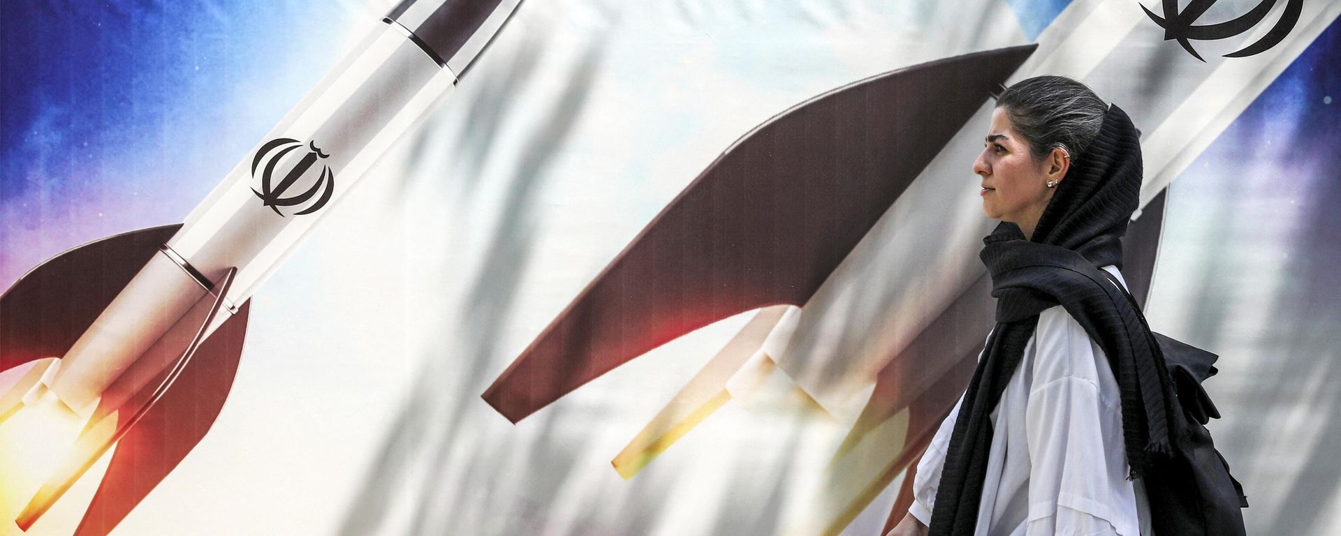 (FILES) A woman walks past a banner depicting launching missiles bearing the emblem of the Islamic Republic of Iran in central Tehran on April 15, 2024. (FILES) A woman walks past a banner depicting launching missiles bearing the emblem of the Islamic Republic of Iran in central Tehran on April 15, 2024. - Sputnik International, 1920, 21.04.2024