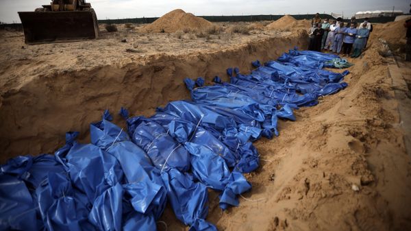 Palestinians pray over bodies of people killed in the Israeli bombardment who were brought from the Shifa hospital before burying them in a mass grave in the town of Khan Younis, southern Gaza Strip on Nov. 22, 2023 - Sputnik International