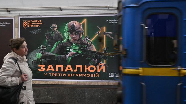 A local resident walks past a recruiting poster for the Ukrainian Third Assault Brigade, made up of fighters from the notorious ultra-right Azov* Regiment, as people take shelter in an underground metro station during an air raid alert in Kyiv on April 23, 2024. - Sputnik International