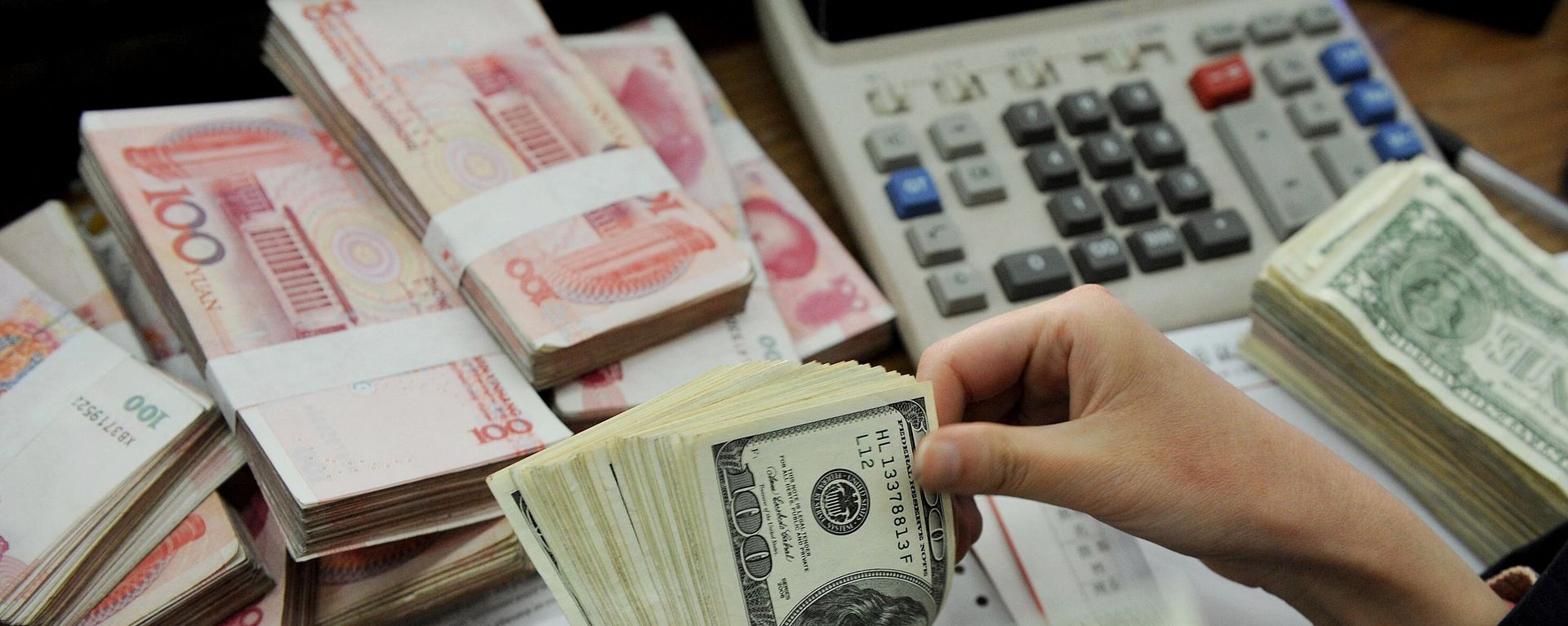 This photo taken n January 16, 2011 shows a bank teller counting stacks of US dollars and Chinese 100-yuan notes at a bank in Hefei, east China's Anhui province. This photo taken n January 16, 2011 shows a bank teller counting stacks of US dollars and Chinese 100-yuan notes at a bank in Hefei, east China's Anhui province. - Sputnik International, 1920, 18.05.2024