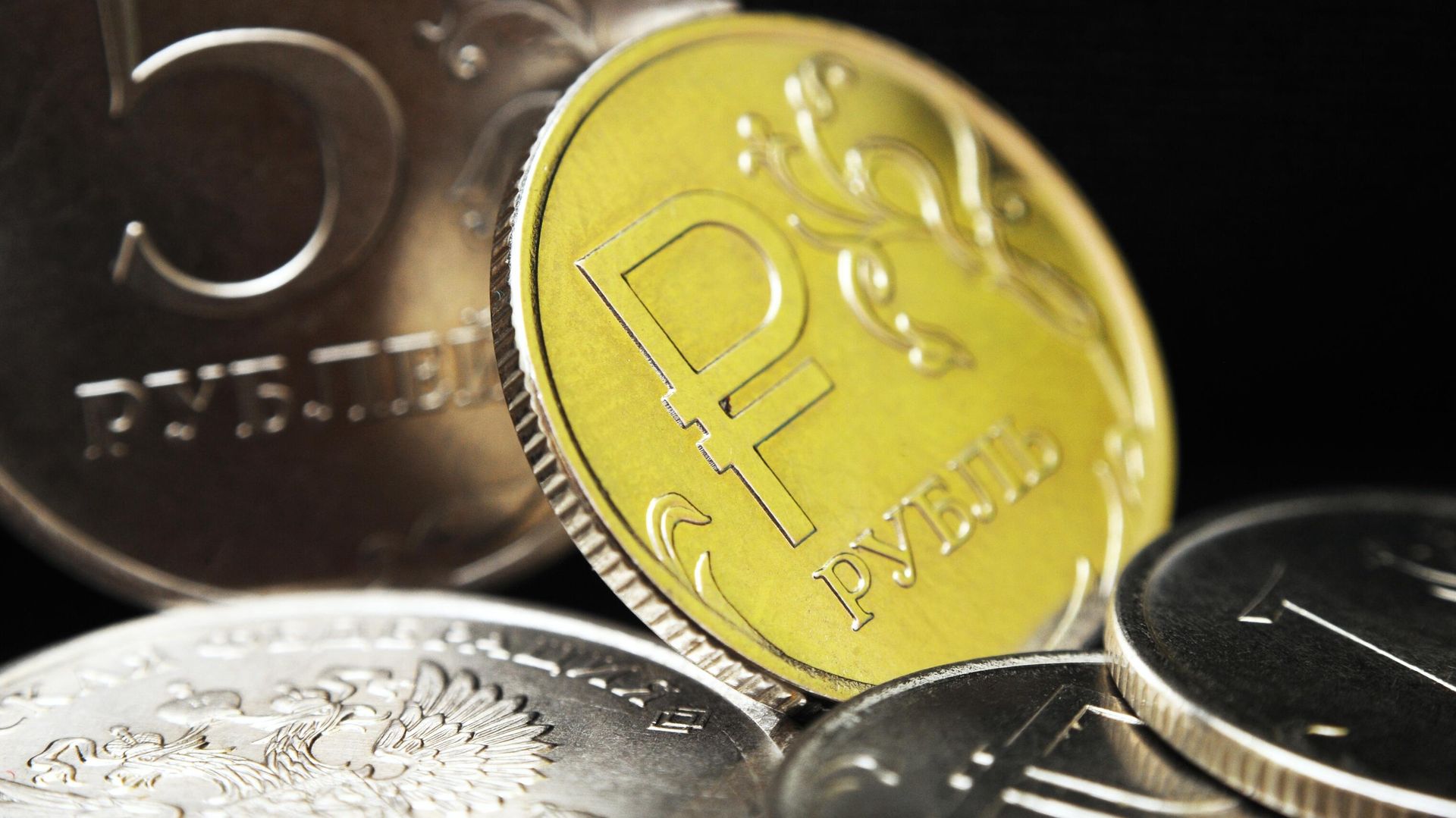 One ruble coin with the symbols of the Russian ruble. In the background is a Russian five-ruble coin - Sputnik International, 1920, 22.10.2024