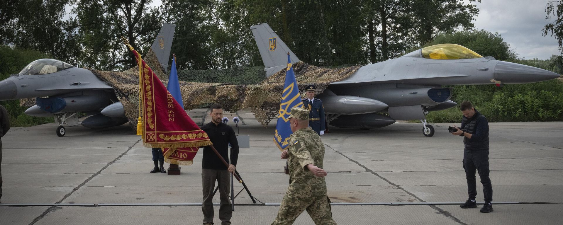 Volodymyr Zelenskyy hands over the flag of a military unit on the occasion of the Air Forces Day against the background of Ukraine's Air Force's F-16 fighter jets in an undisclosed location in Ukraine, Sunday, Aug. 4, 2024.  - Sputnik International, 1920, 17.02.2026