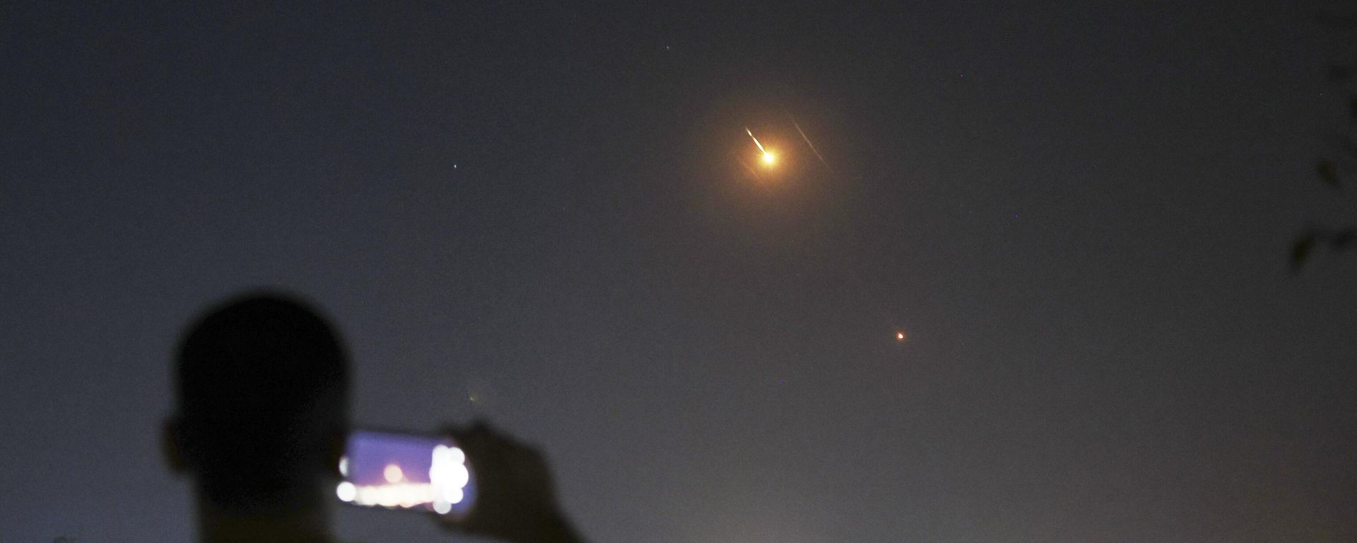 A man takes a cellphone photo as missiles fired from Iran toward Israel fly over Syrian territory in Damascus - Sputnik International, 1920, 18.07.2025