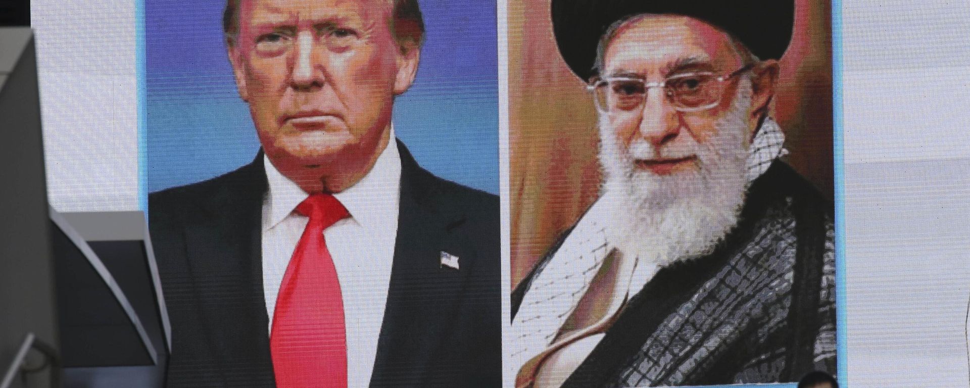 A man walks by a huge screen showing U.S. President Donald Trump, left, and Iranian Supreme Leader Ayatollah Ali Khamenei, in Tokyo, Wednesday, Jan. 8, 2020. Iran struck back at the United States early Wednesday for killing a top Revolutionary Guards commander, firing a series of ballistic missiles at two military bases in Iraq housing American troops in a major escalation between the two longtime foes. (AP Photo/Koji Sasahara) - Sputnik International, 1920, 21.02.2026